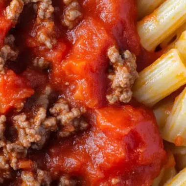 A close-up of pasta with meat sauce and diced tomatoes.