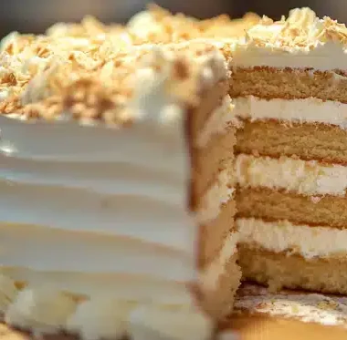 A partially sliced cake with cream and coconut flakes on top.
