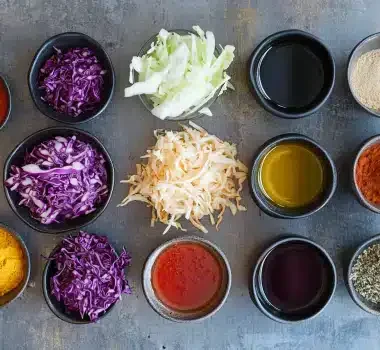 A variety of colorful spices and chopped vegetables arranged in bowls on a textured surface.
