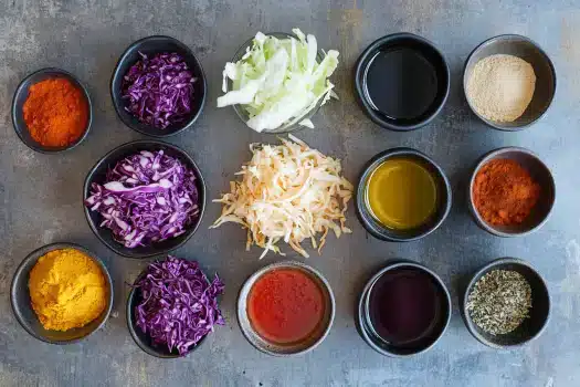 A variety of colorful spices and chopped vegetables arranged in bowls on a textured surface.