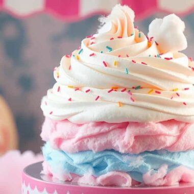 A whimsical dessert made of layers of pink and blue cotton candy topped with white frosting and sprinkles.