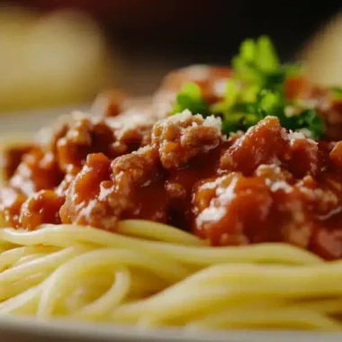 A plate of spaghetti topped with meat sauce and parsley garnish.