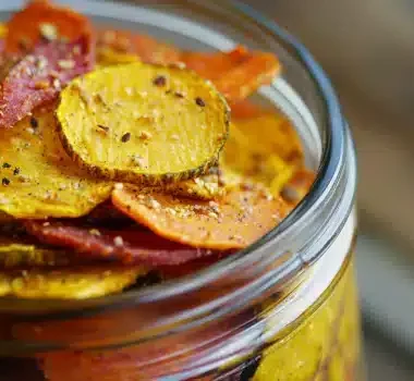 A close-up of colorful vegetable chips in a glass jar.