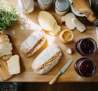 A wooden table adorned with bread, jars of jam, and a plant in bright light.