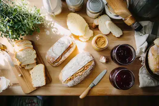 A wooden table adorned with bread, jars of jam, and a plant in bright light.