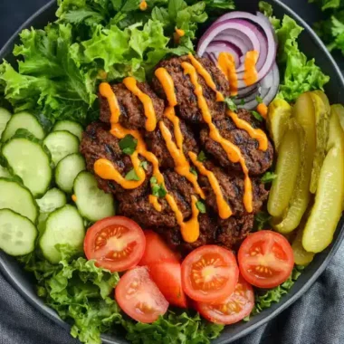 A vibrant salad bowl filled with lettuce, cucumbers, tomatoes, pickles, and seasoned meat drizzled with orange sauce.