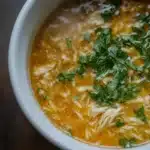 A close-up image of a bowl of chicken orzo soup garnished with fresh parsley.