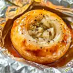 A close-up overhead image of a roasted onion in foil.